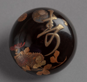 Circular lacquer netsuke with design of chrysanthemums and long life symbol.