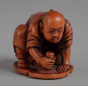 Wooden netsuke carving of man in kimono on hands and knees polishing the floor.