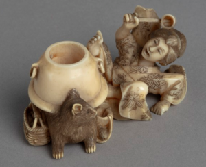 Ivory carving of a Japanese woman falling back in surprise as a water pot transforms into a raccoon.