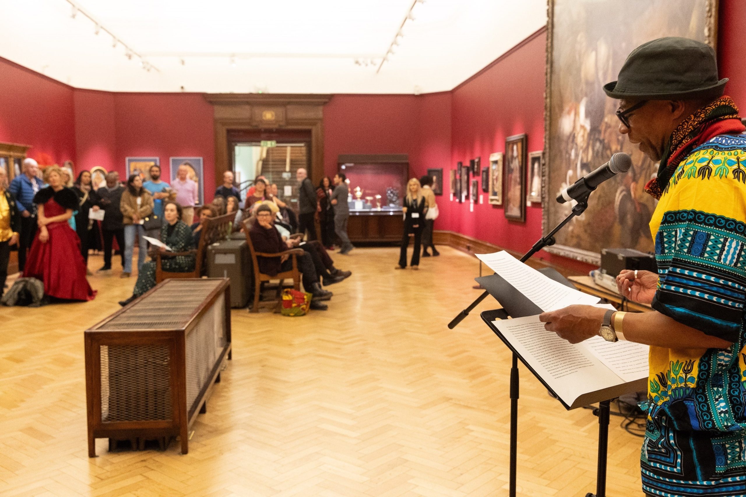 Black man talking to a crowd through a microphone in a gallery space.