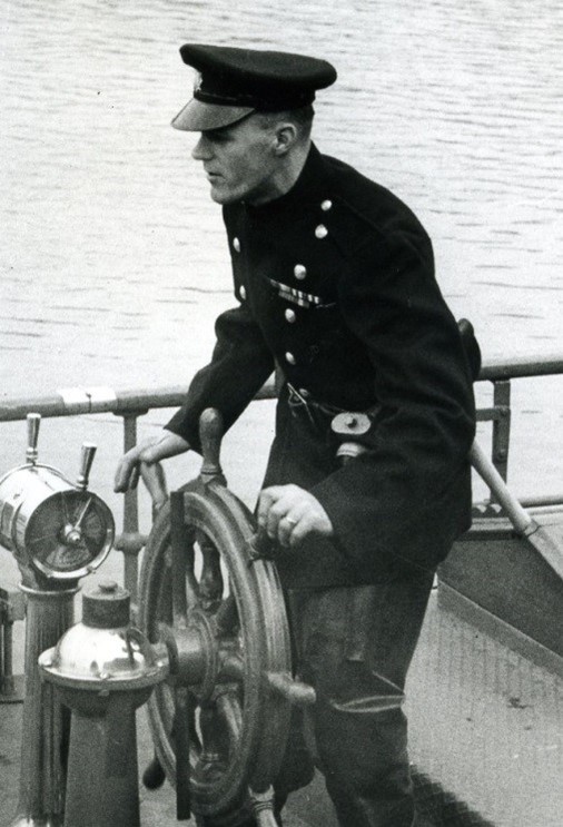 A helmsman in black naval uniform steers the ship.